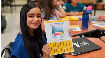 Student participating in an Erika's Lighthouse mental health education program while holding a classroom activity focused on help-seeking and trusted adult support.