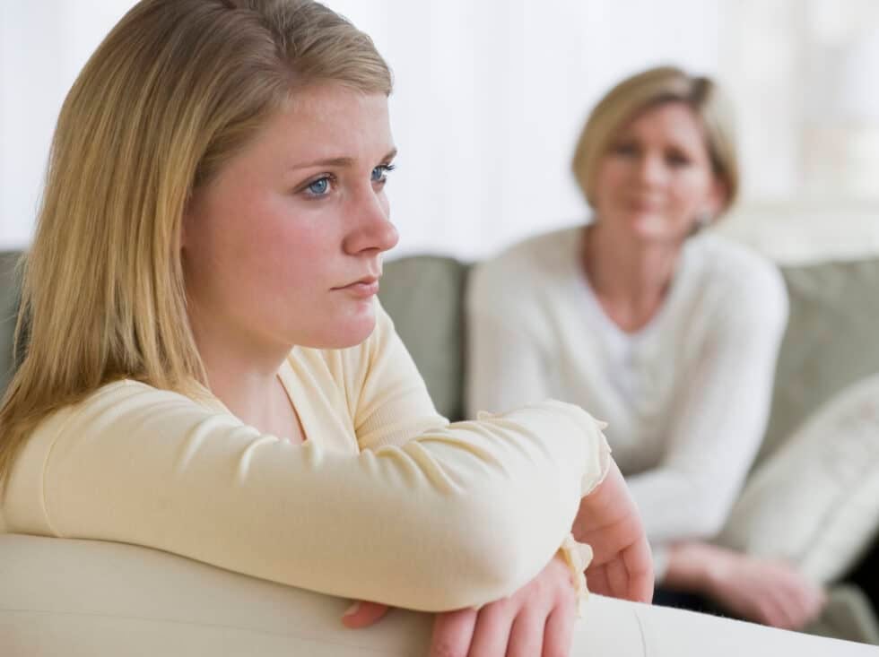 young woman looking into distance with parent in distance looking at her