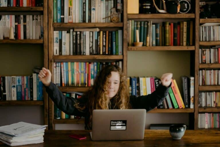 young person looking at a computer with her arms up