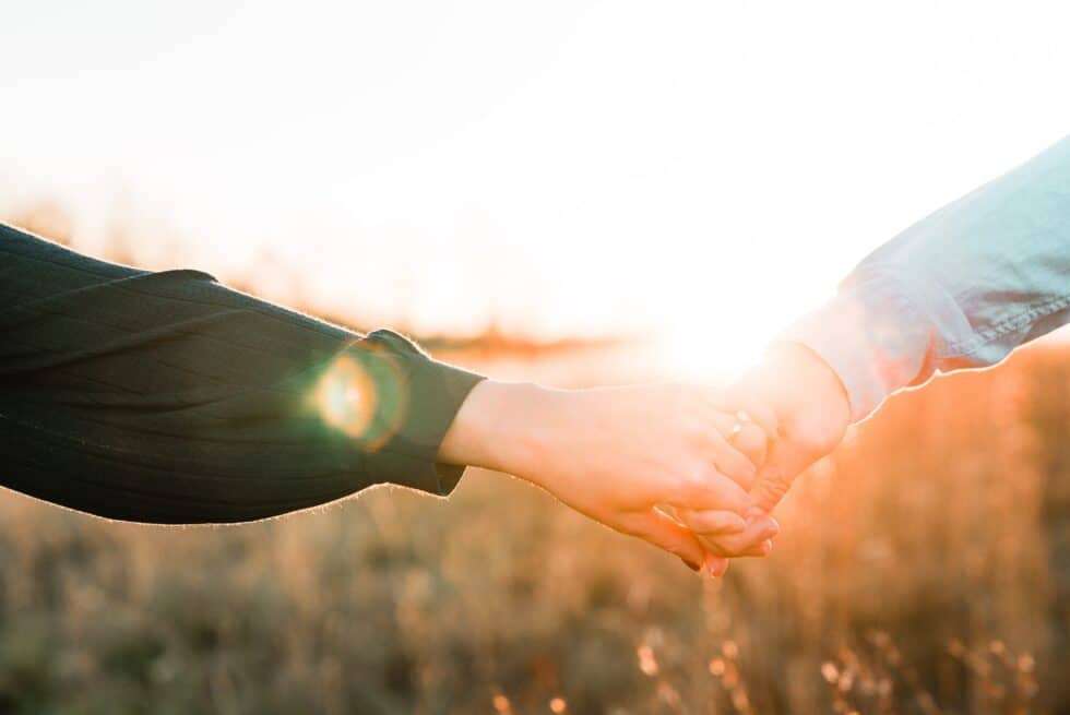 two people holding hands in a field with sunlight behind