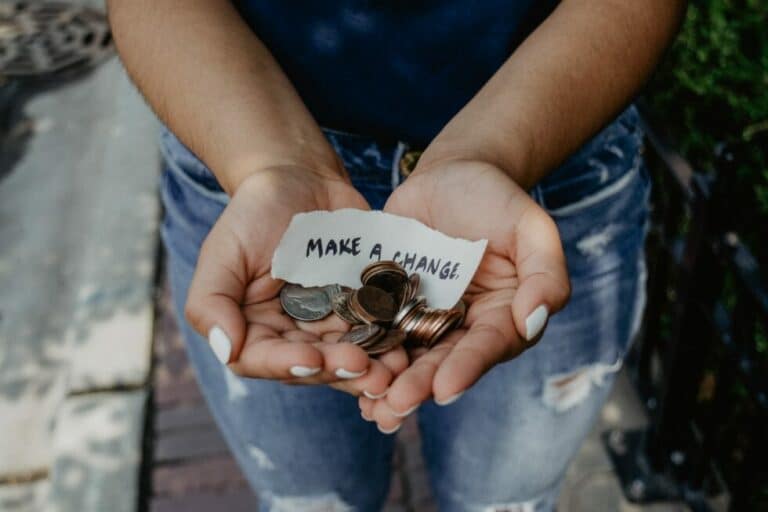 person holding coins in hands with note that says "Make a Change"
