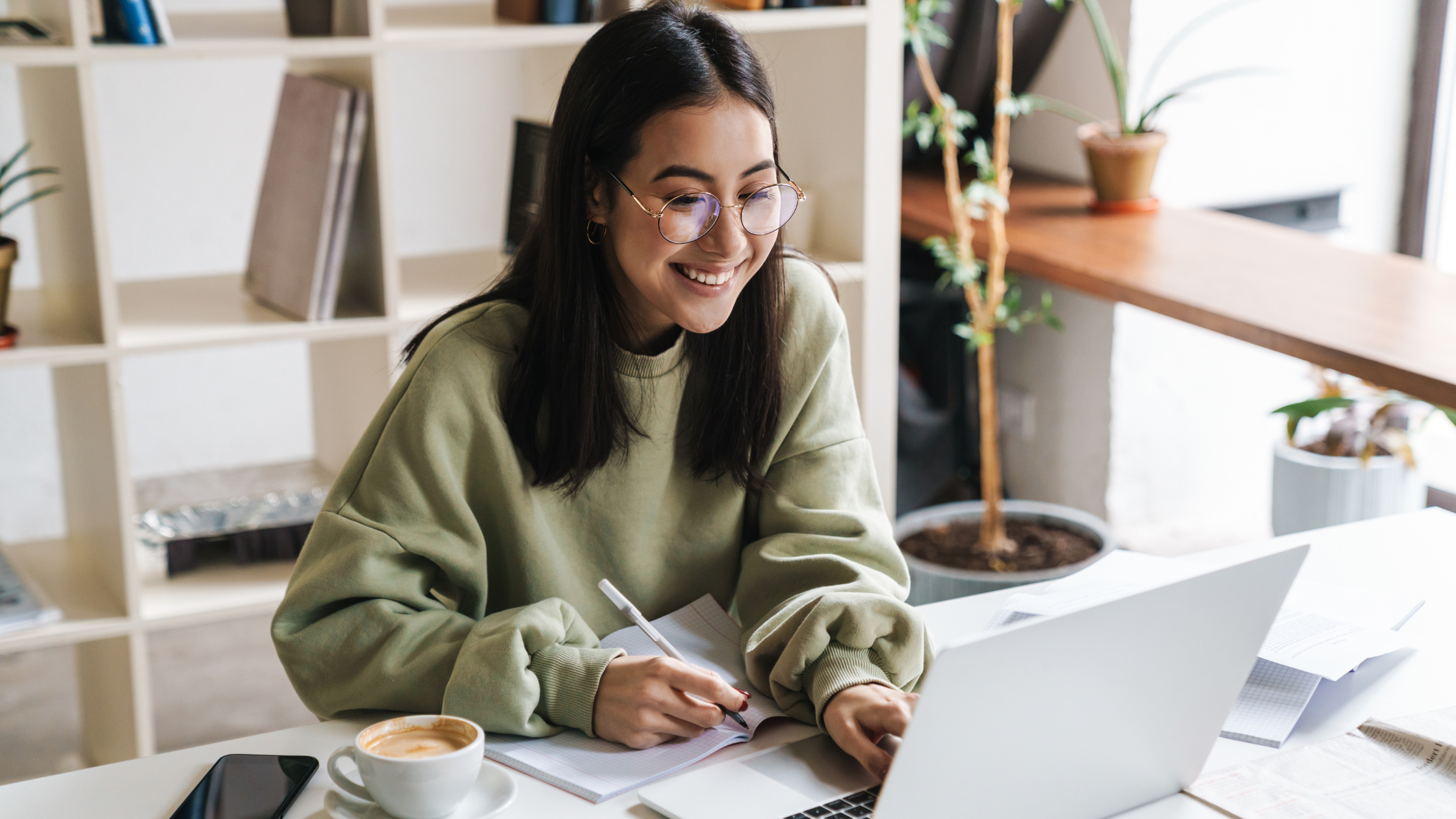A school social worker smiles while using her laptop to explore free Tier-1 mental health resources inside a bright, welcoming office.