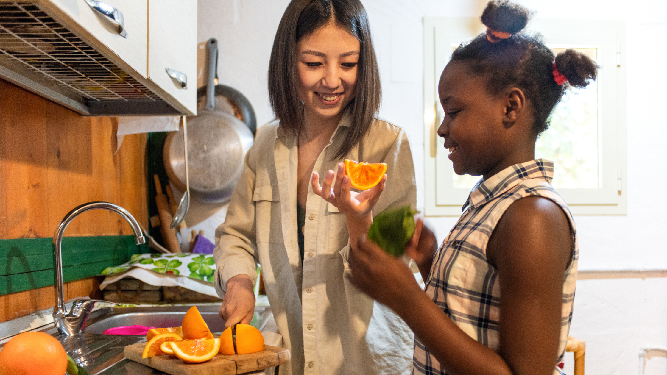 Woman and child smiling while slicing fresh oranges in a kitchen.